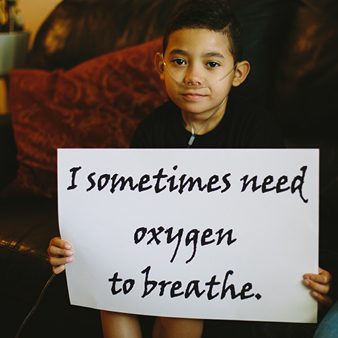 A boy with oxygen supply tube holding a sign saying 
