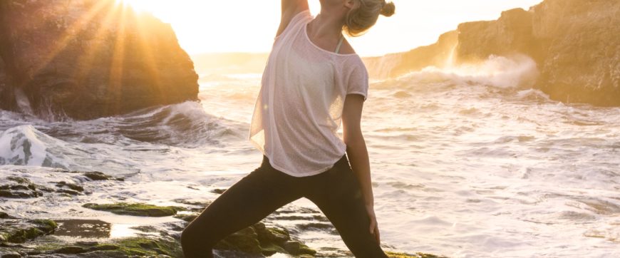 Young woman with CF strikes a yoga pose as waves break behind her.
