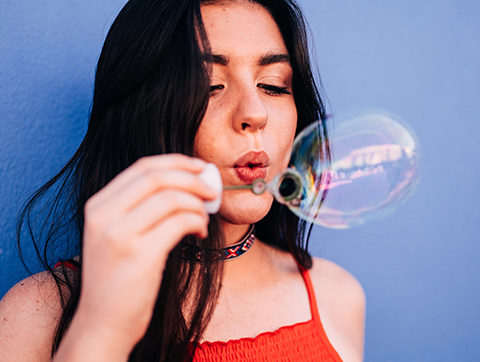 Girl in a red dress with long black hair blowing bubbles